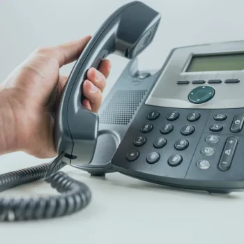 Main décrochant le combiné d'un téléphone de bureau